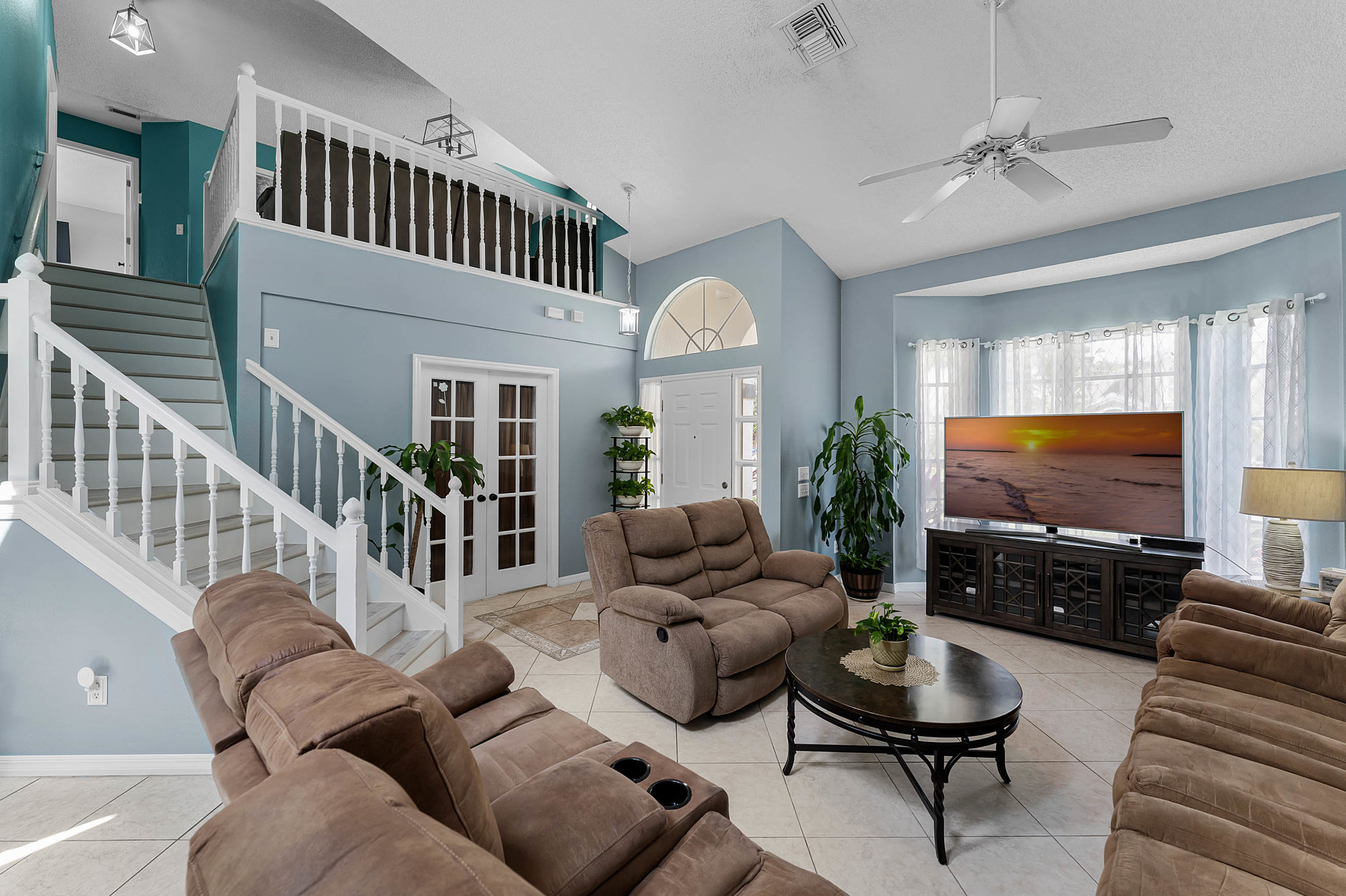 living space with light blue walls, brown couches and white railing going upstairs